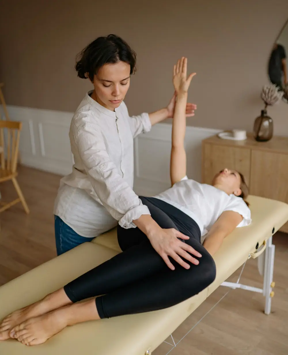 A physical therapist guides a female patient through a rehabilitation exercise on a treatment table, focusing on arm and torso rotation.