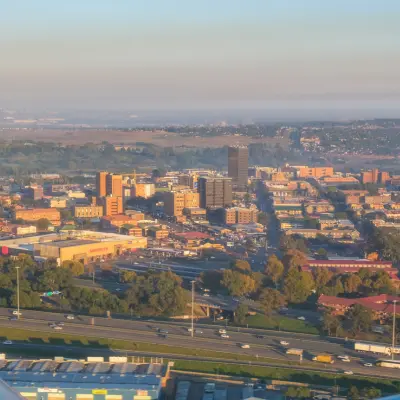 An aerial view of a sprawling urban landscape with a highway, buildings, and distant hazy hills under a clear sky.