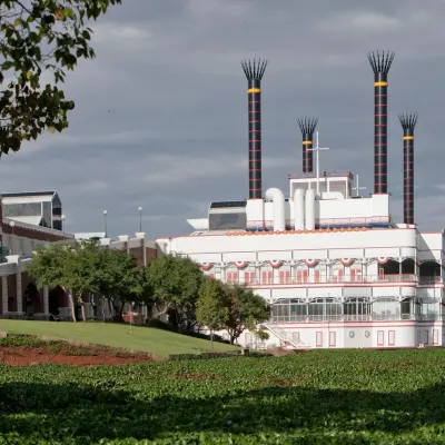 A large, multi-decked boat-like building with prominent smokestacks and a festive facade, surrounded by water plants and green landscaping.