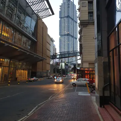 A street view in an urban area with tall buildings, a pedestrian bridge, and cars on the road at dusk.