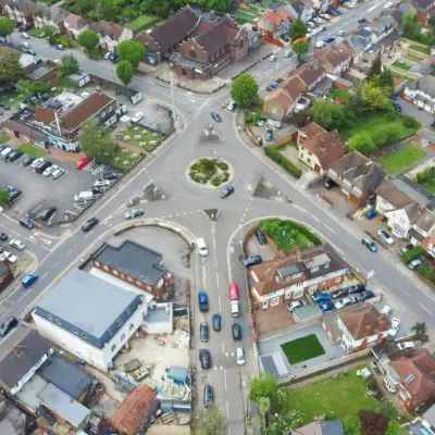 n aerial view of a busy traffic roundabout in a town, surrounded by residential houses and some commercial buildings.