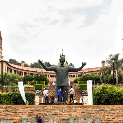 The large bronze statue of Nelson Mandela at the Union Buildings in Pretoria, with people around its base and grand terraced gardens.