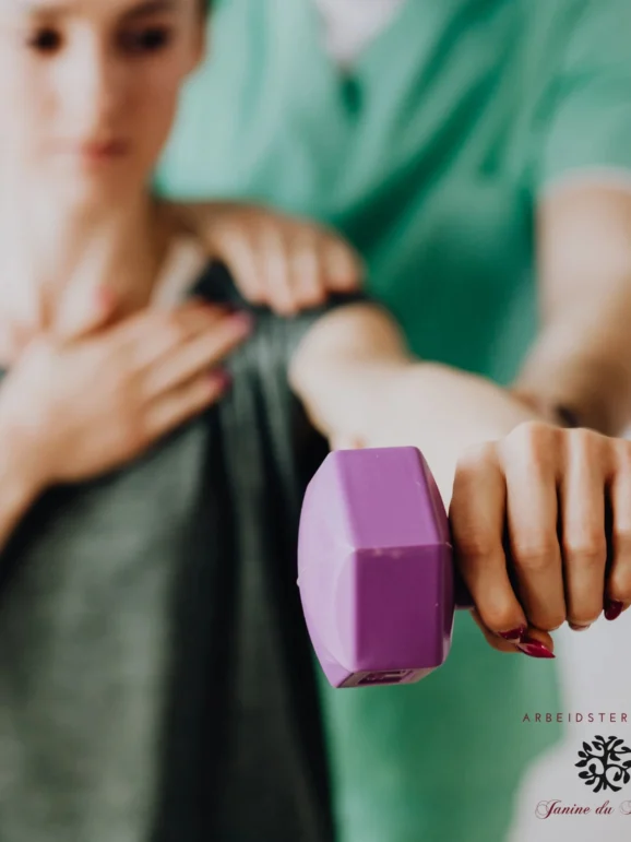 A physical therapist in green scrubs assisting a female patient with shoulder rehabilitation using a purple dumbbell.