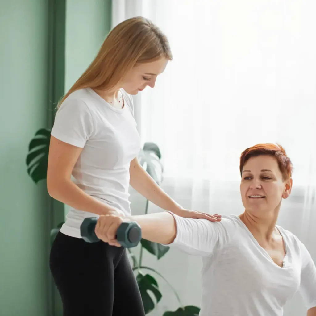 A physical therapist assists an older woman with a shoulder exercise using a light dumbbell.